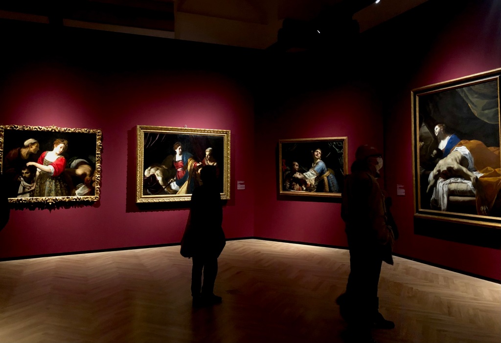 A shot of one of the galleries in the exhibition. Two walls are visible, hung with four paintings all depicting Judith in various stages of removing Holofernes' head.