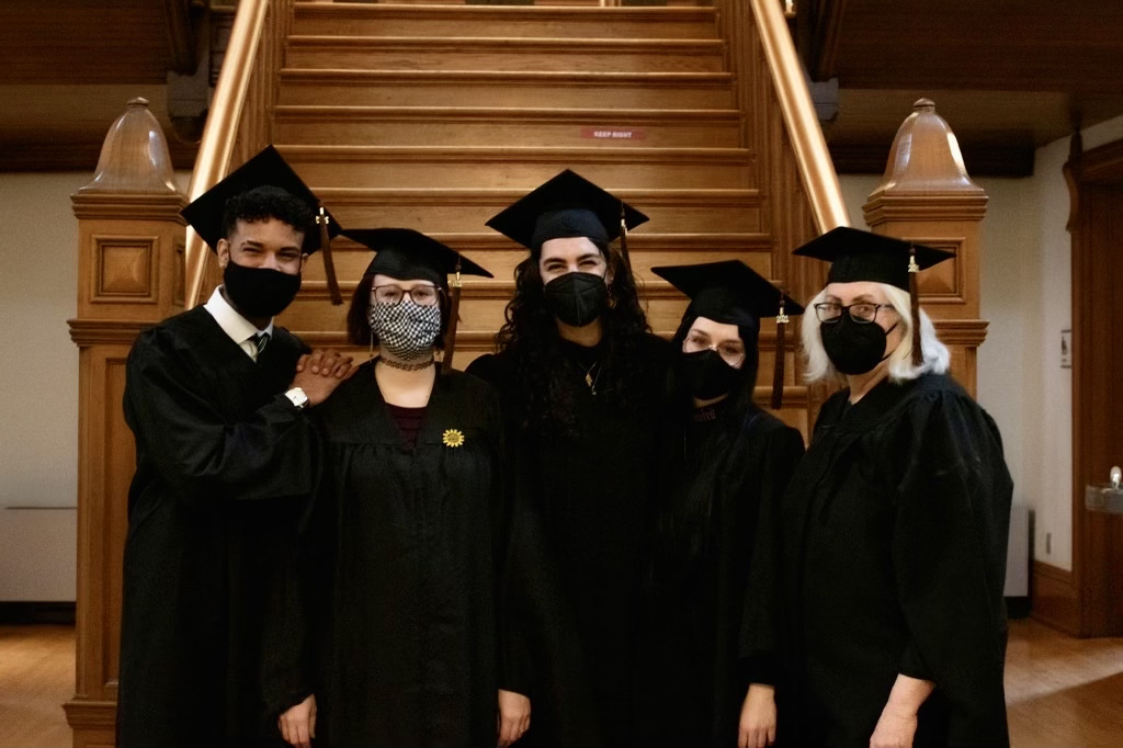 A group of five graduates pose in their caps and gowns, about to receive their MFA diplomas.